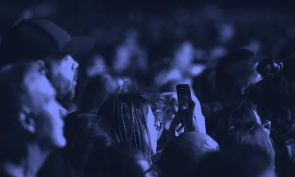 A crowd of people looking down at their glowing smartphones in the dark.