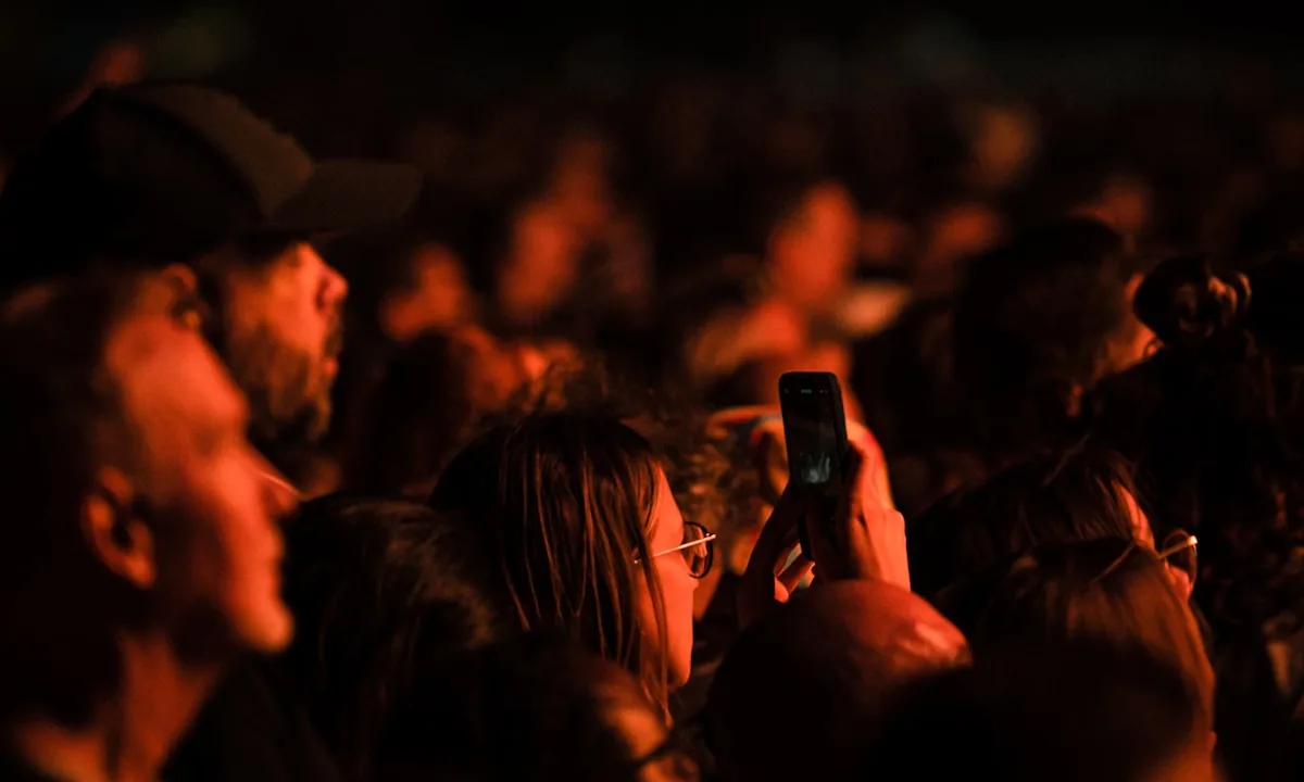 A crowd of people looking down at their glowing smartphones in the dark.