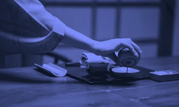 Pouring hot tea into a ceramic cup on a wooden table.