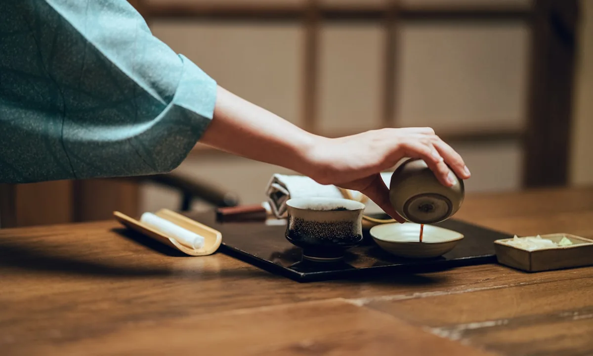 Pouring hot tea into a ceramic cup on a wooden table.