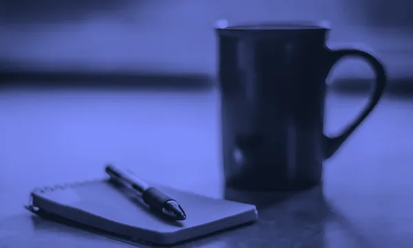 A neat workspace with a notebook, pen, and warm cup of tea