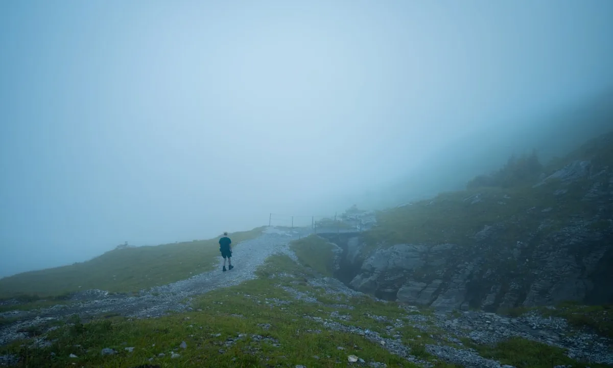 A lone traveler walking along a winding mountain trail shrouded in morning fog